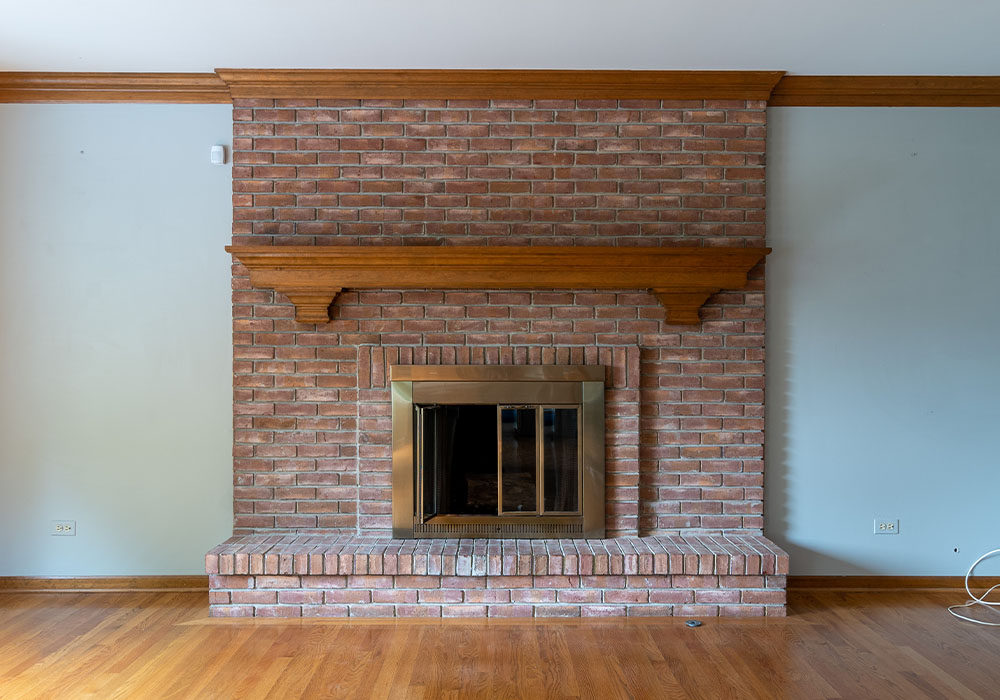 Brick fireplace with wooden mantel in a room with hardwood floors. Classic design and cozy atmosphere.