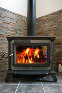 Wood-burning stove with a roaring fire against a brick wall background.