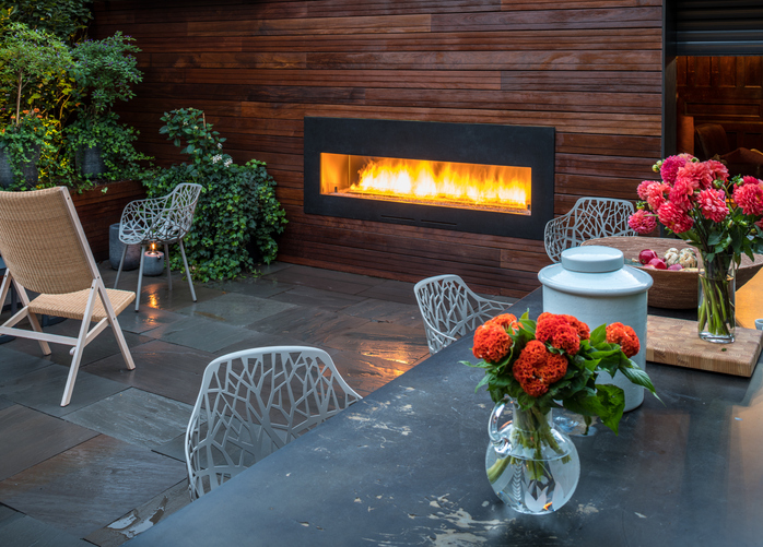 Outdoor patio with modern fireplace, sleek chairs, and vibrant flowers on table. Cozy ambiance for relaxation.