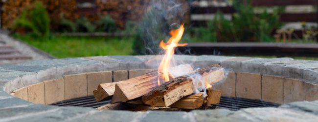 Crackling firewood burning in a stone fire pit in a backyard setting.