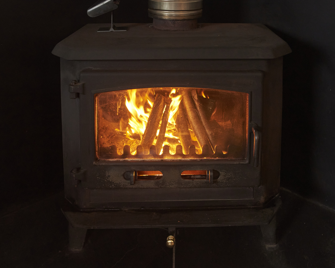 Wood-burning stove with roaring fire, casting warm glow on surrounding area.