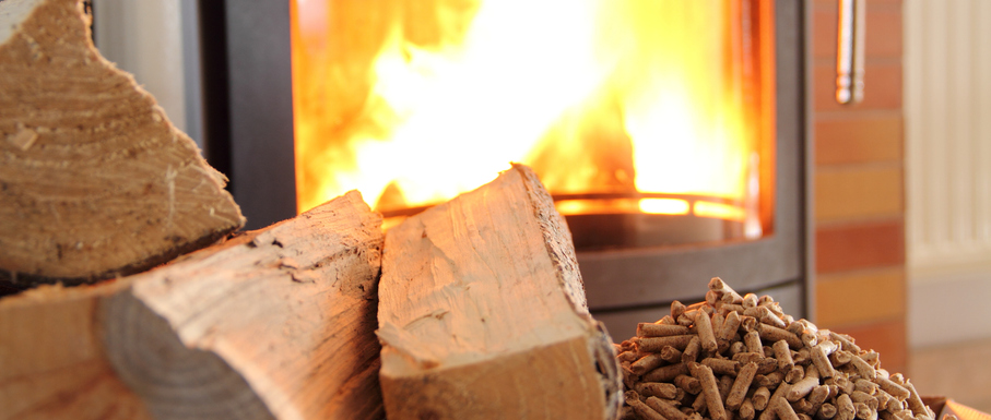 Wood logs and pellets in front of a burning stove, highlighting eco-friendly heating options.
