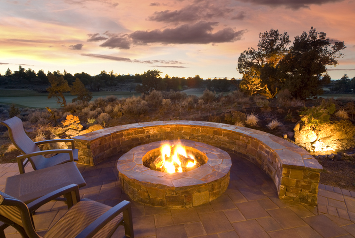 Outdoor stone fire pit with cozy seating at sunset, surrounded by natural landscape.